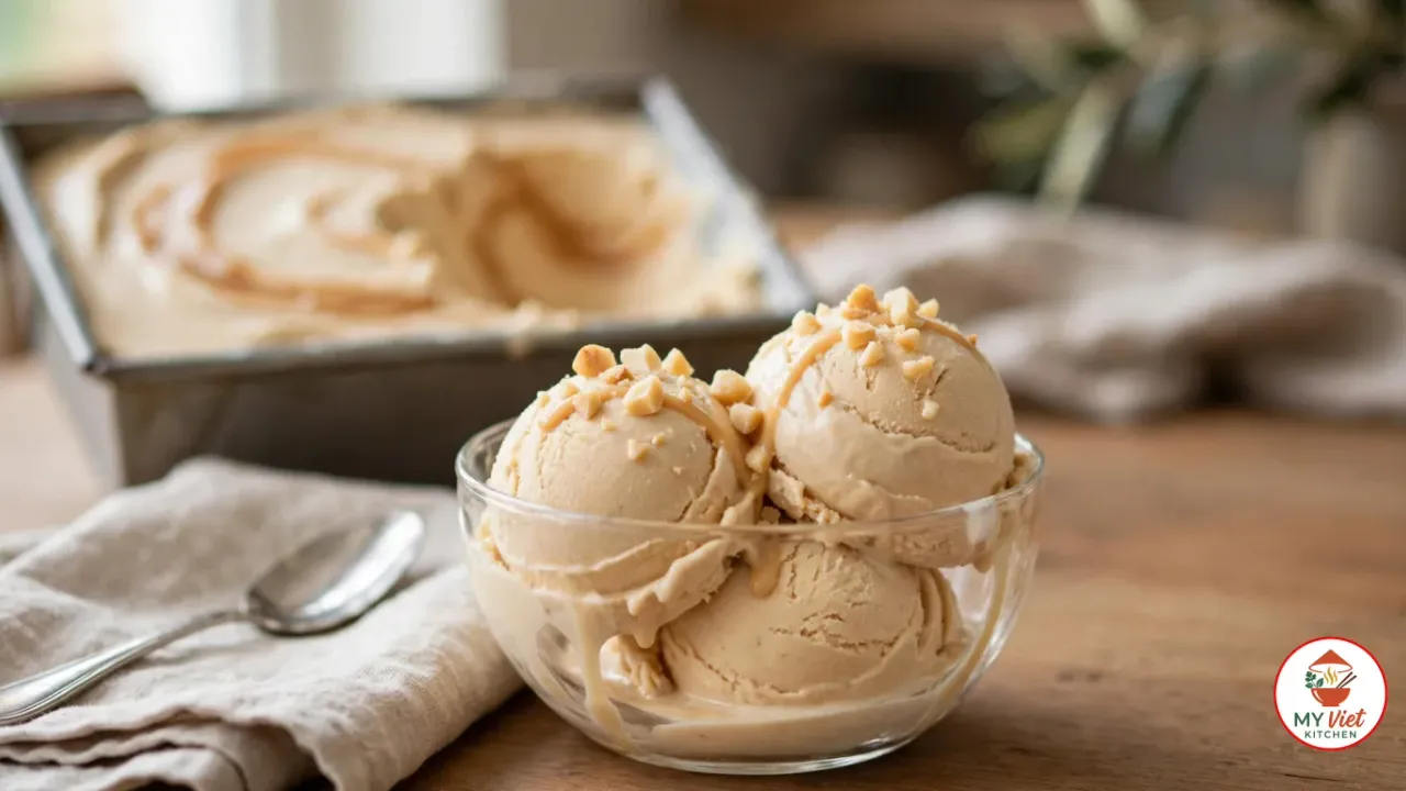 Three scoops of Amarula ice cream with a caramel drizzle and chopped macadamia nuts in a glass bowl, with the caramel-swirled loaf pan behind