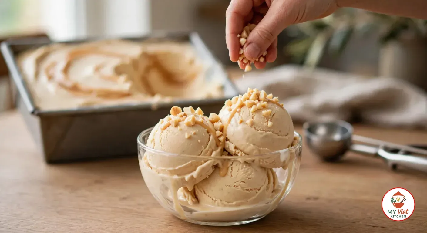 Sprinkling chopped macadamia nuts over scoops of Amarula ice cream in a glass bowl, with the loaf pan and an ice cream scoop behind